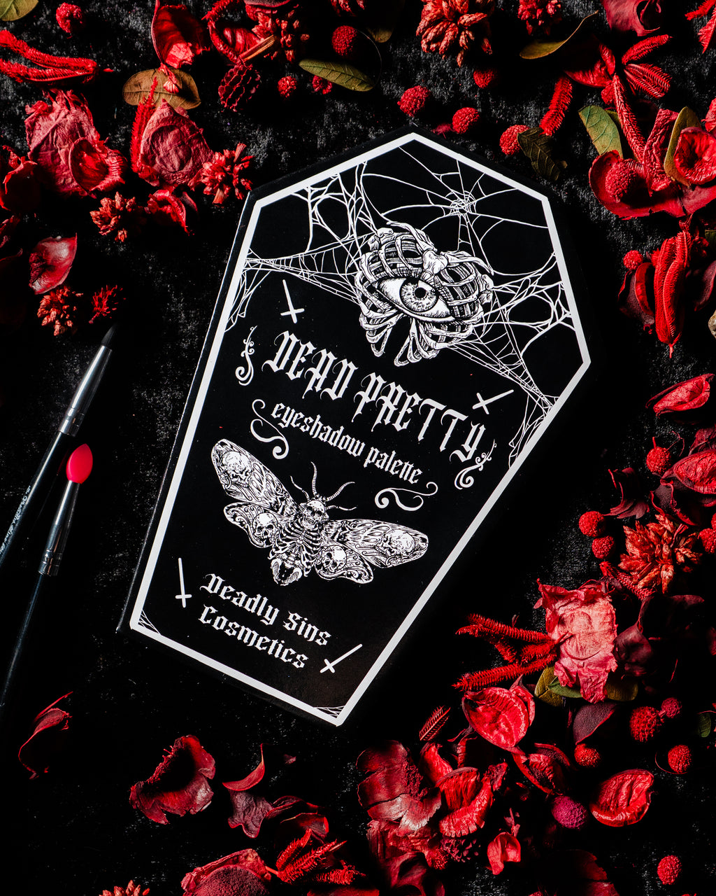 Deadly Sins Cosmetics 'Dead Pretty' eyeshadow palette with moths and spider web design on a dark background with red a gothic style.